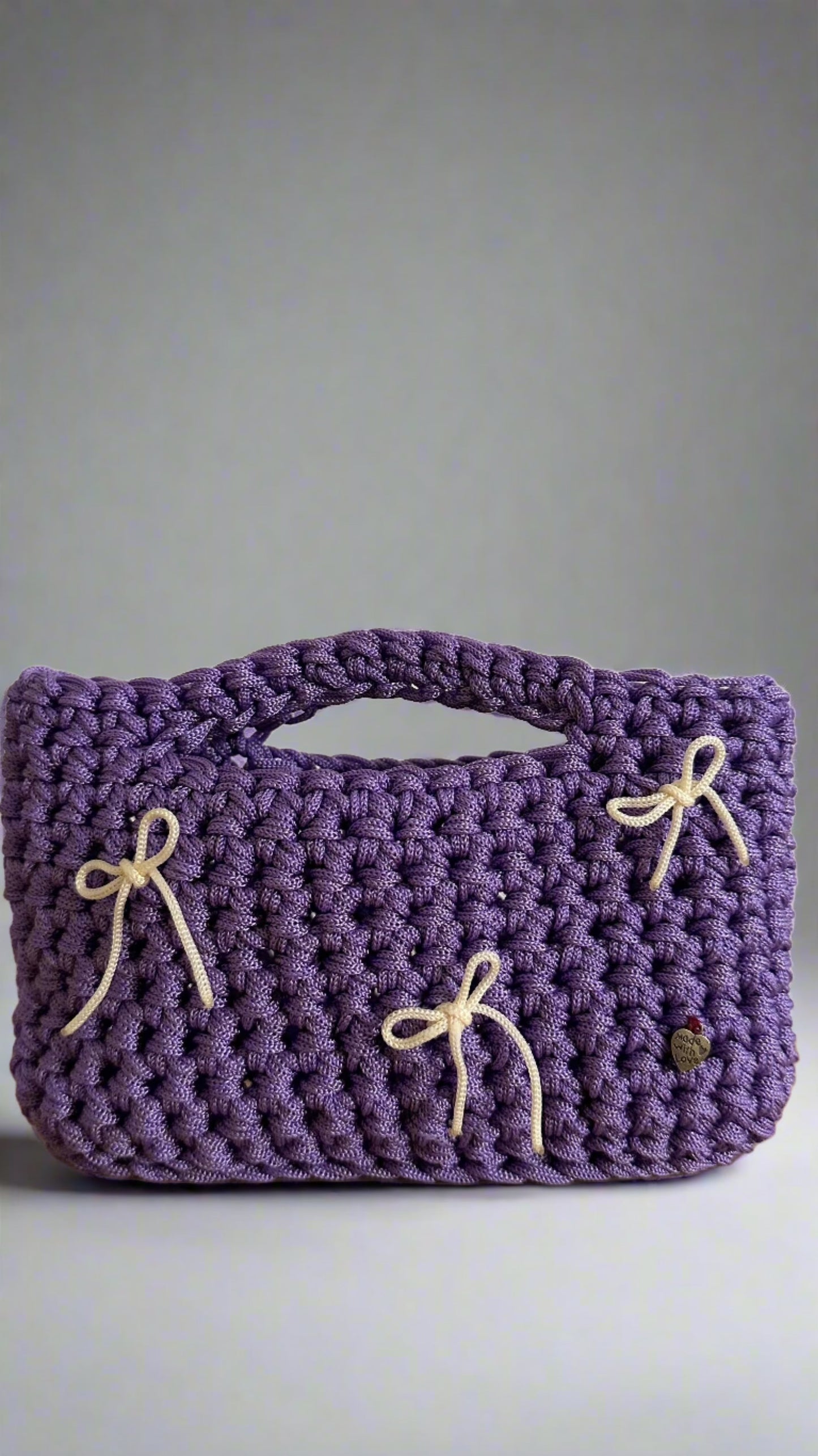 <img ="creaturina_bag.png" alt="Luglina mini bag uncinetto fatta a mano colore lilla con fiocchetti panna">